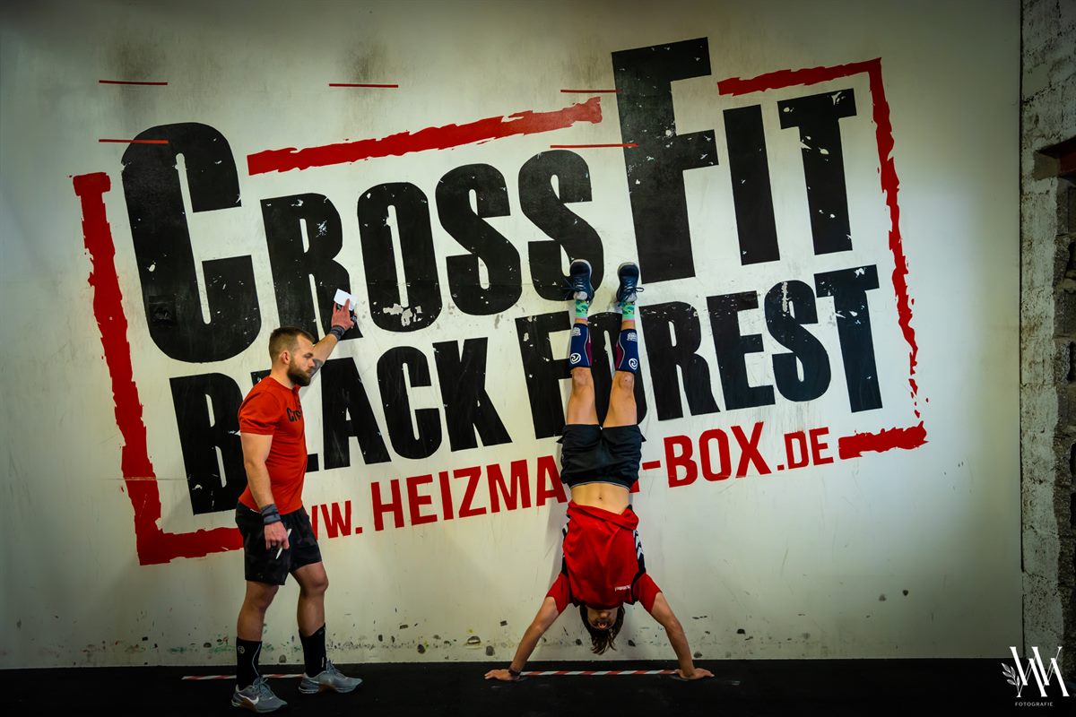 Handstand auf der Trainingsfläche, daneben ein Coach